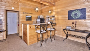 L’intérieur d’un chalet en bois comprend un coin cuisine, une table à manger avec des chaises, un petit comptoir-bar et un élément décoratif mural.