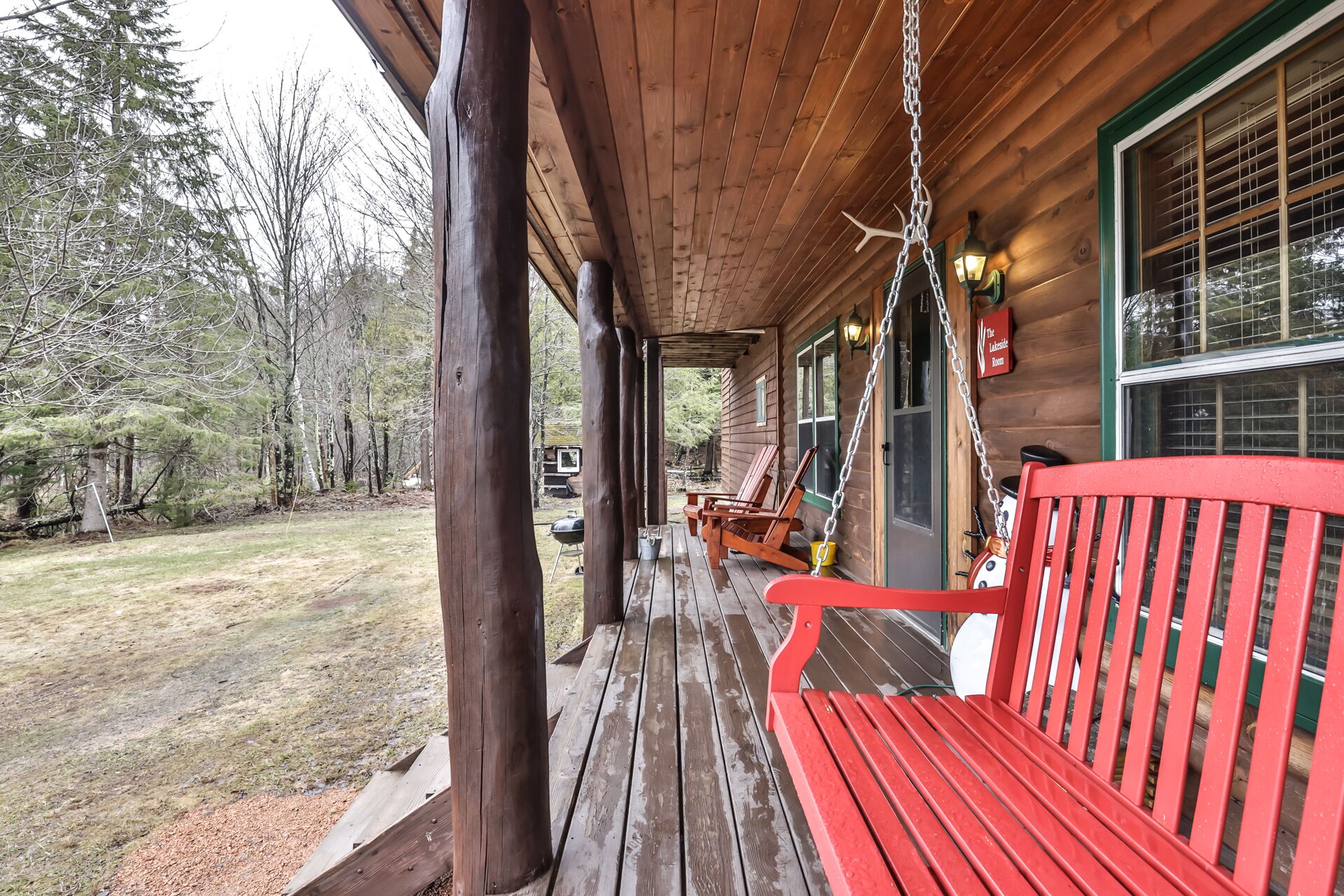 A wooden porch with a red bench, a hanging light fixture, and a sign reading "The Lodge Room."