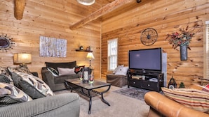 L’intérieur chaleureux d’un chalet en bois, avec un canapé, un fauteuil et un téléviseur fixés à un mur en bois.