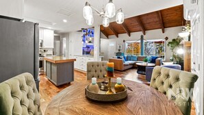 A spacious living area with a round wooden coffee table, a tufted sofa, and a dining table with candles. - Luxury Home—Hot Tub, Fire Table, Office, Stunning Lake Views, 15 Miles to Silverwood, 2 to Beach! (Hayden)