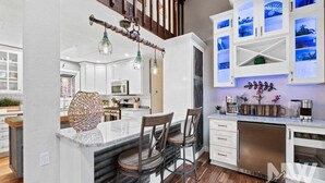 A modern kitchen with white cabinets, a marble island, and bar stools. - Luxury Home—Hot Tub, Fire Table, Office, Stunning Lake Views, 15 Miles to Silverwood, 2 to Beach! (Hayden)