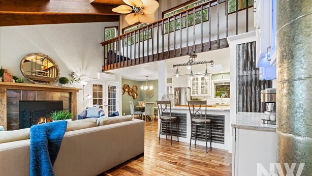 A spacious living area with a high ceiling, wooden flooring, a fireplace, a large sofa, and a dining area with a bar. - Luxury Home—Hot Tub, Fire Table, Office, Stunning Lake Views, 15 Miles to Silverwood, 2 to Beach! (Hayden)
