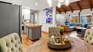 A spacious living area with a round wooden coffee table, a tufted sofa, and a dining table with candles.