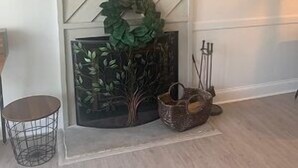 Una sala de estar moderna con un televisor de pantalla plana grande montado en una pared blanca con un patrón diagonal. Hay obras de arte enmarcadas en la pared, una guirnalda decorativa y una pequeña mesa redonda con una base de alambre metálico.