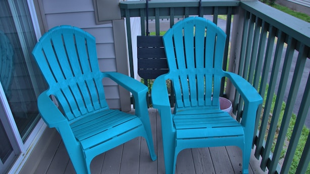Dos sillas Adirondack color turquesa en una terraza de madera con barandilla.