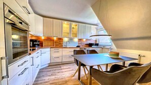 Una cocina moderna con armarios blancos, horno empotrado y una zona de comedor con mesa y sillas.