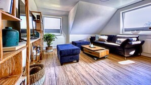 Un loft moderno con techo inclinado, suelo de madera, un sofá azul, una mesa de centro de madera y una estantería.