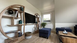En moderne stue med en træbogreol, et fladskærms-tv, en blå sofa og et sofabord.