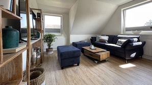 En moderne stue i loftstil med skråvægge, en mørkeblå sofa, et træbord og en bogreol.