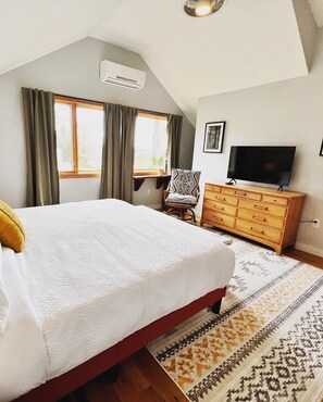 Une chambre à coucher avec un grand lit, une commode en bois, un téléviseur et une fenêtre avec des rideaux.