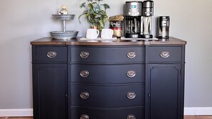Una encimera de cocina con una cafetera, una taza y un paquete de café. Hay dos adornos de pared, uno que dice “Coffee” y el otro “Coffee bar”.