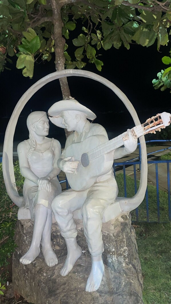 Una escultura de un hombre tocando guitarra y una mujer sentada a su lado, ambos sobre una roca.