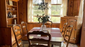 Uma sala de jantar de madeira com uma mesa posta para quatro pessoas, rodeada por cadeiras. Um candeeiro pendente em forma de estrela está sobre a mesa.