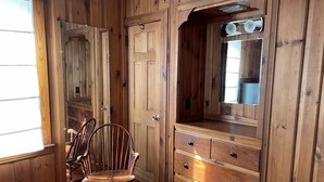 Quarto com painéis de madeira, uma cadeira de madeira, uma cômoda com gavetas e um espelho.