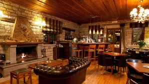 A cozy interior with a stone fireplace, leather sofa, wooden dining table, and bar area. - Nisista Lodge Mountain View (Arta)