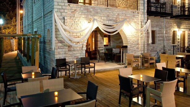 A stone building with a wooden deck, outdoor seating, and a balcony. - Nisista Lodge Mountain View (Arta)