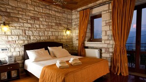 A room with a stone wall, a wooden bed with white bedding, two bedside tables, a nightstand, and a window with curtains. - Nisista Lodge Mountain View (Arta)