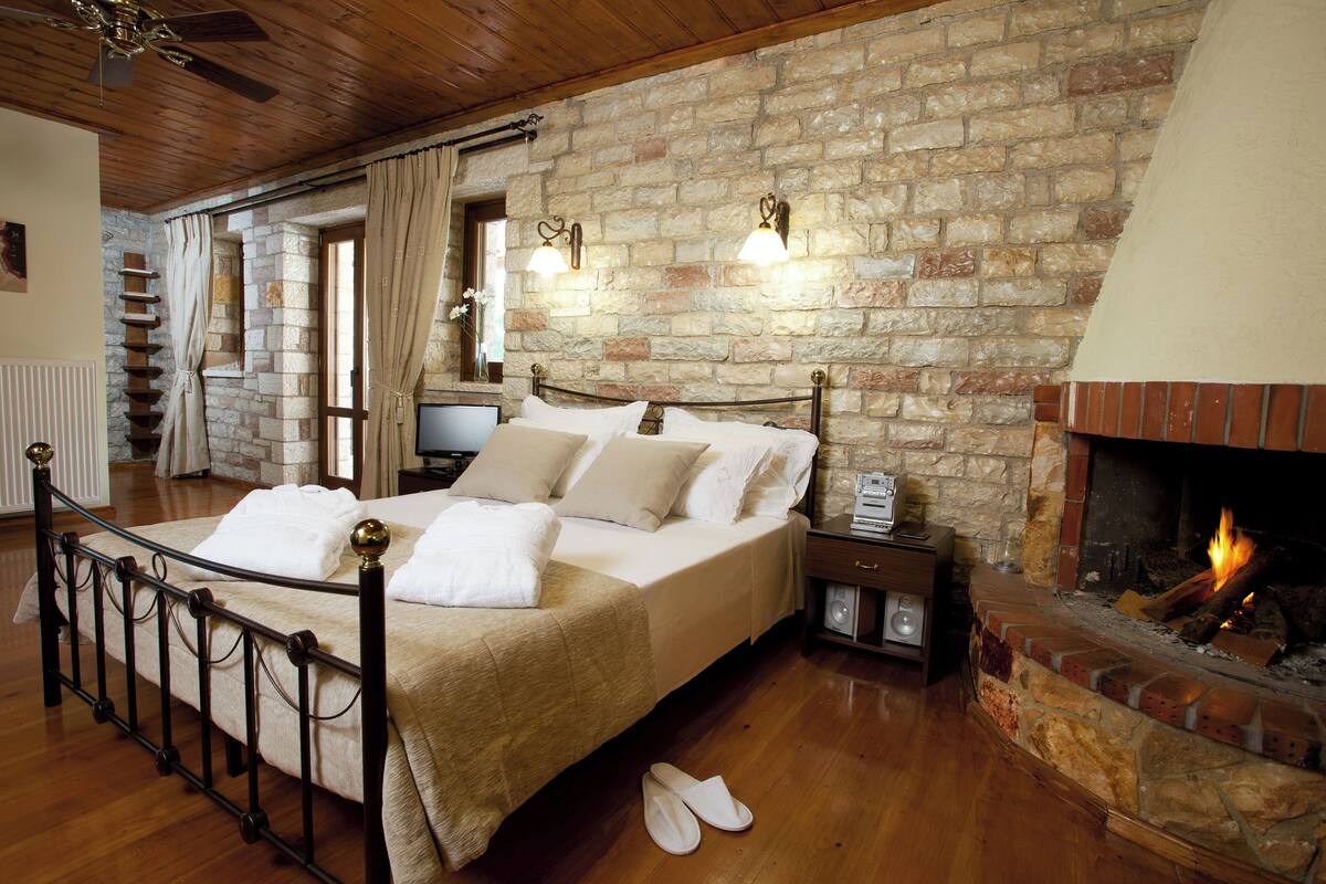 Ein Schlafzimmer mit Steinwand, Kamin, einem Bett mit weißen Leinen und Holzboden.