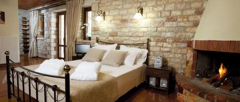 Un dormitorio con pared de piedra, chimenea, cama con ropa blanca y suelo de madera.