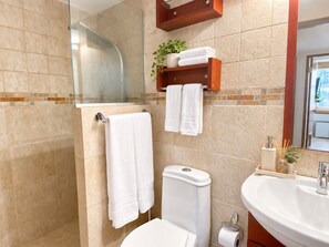 Un bagno con box doccia in vetro, un water, un lavandino con specchio e uno scaffale con asciugamani e una pianta.
