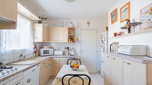 A kitchen with wooden cabinets, a dining table with a floral tablecloth, and a fruit bowl. - Ty Yann - proche plage (Carantec)