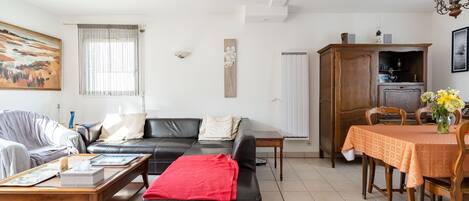 A living room with a black sofa, a wooden coffee table, a dining table with chairs, and a painting on the wall.