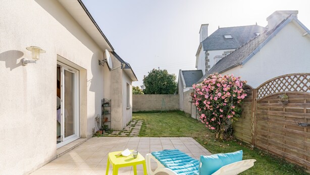 A patio with a yellow table, a white lounge chair with a blue cushion, and a wooden fence with pink flowers. - Ty Yann - proche plage (Carantec)