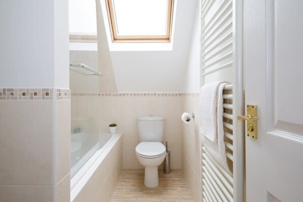 Une petite salle de bain avec un puits de lumière, des toilettes, une baignoire et un porte-serviettes.