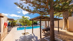 Ein Poolbereich mit Holzterrasse, überdachter Sitzgelegenheit und einem kleinen Baum.