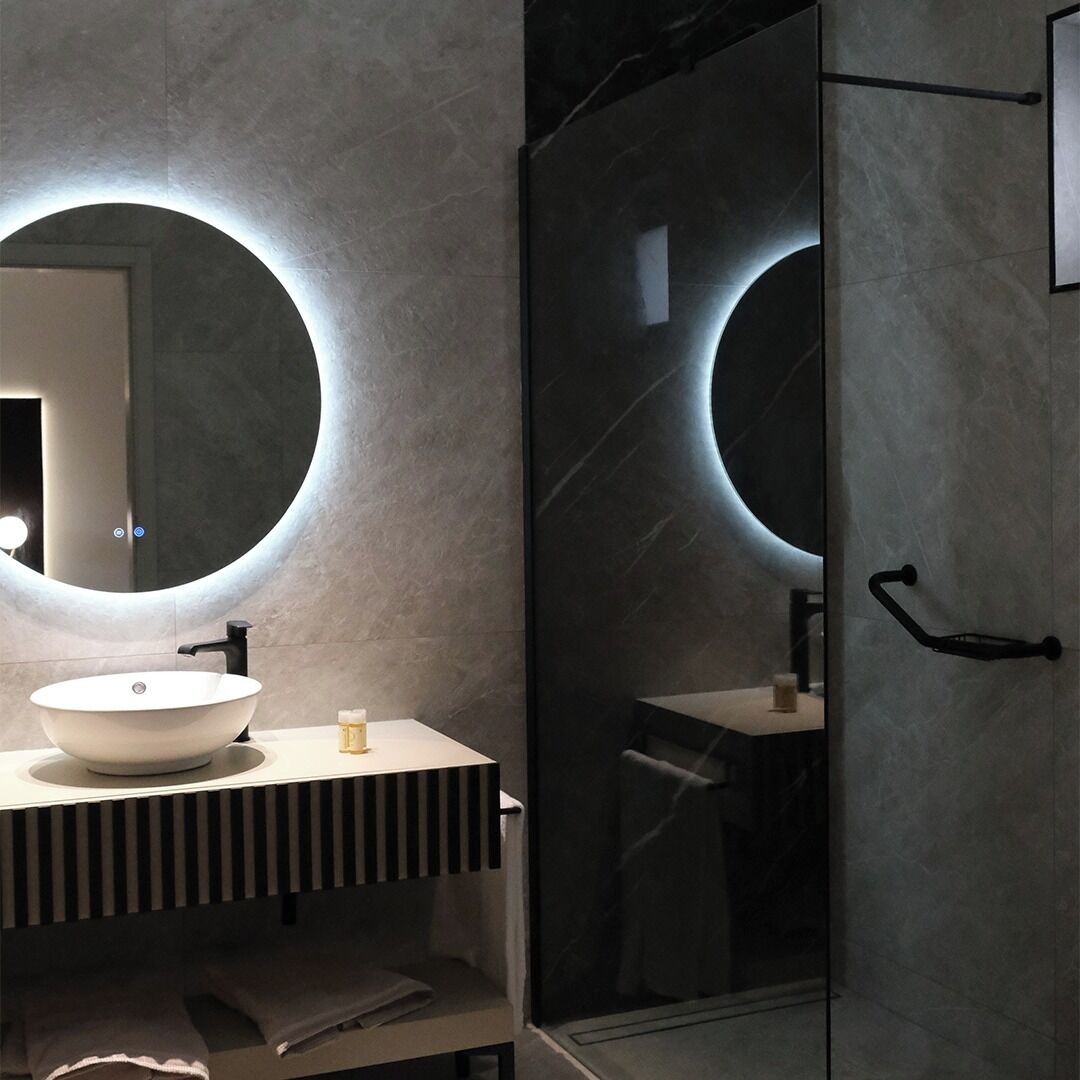 Une salle de bain moderne avec un grand miroir rond, un lavabo et une douche à parois de verre.