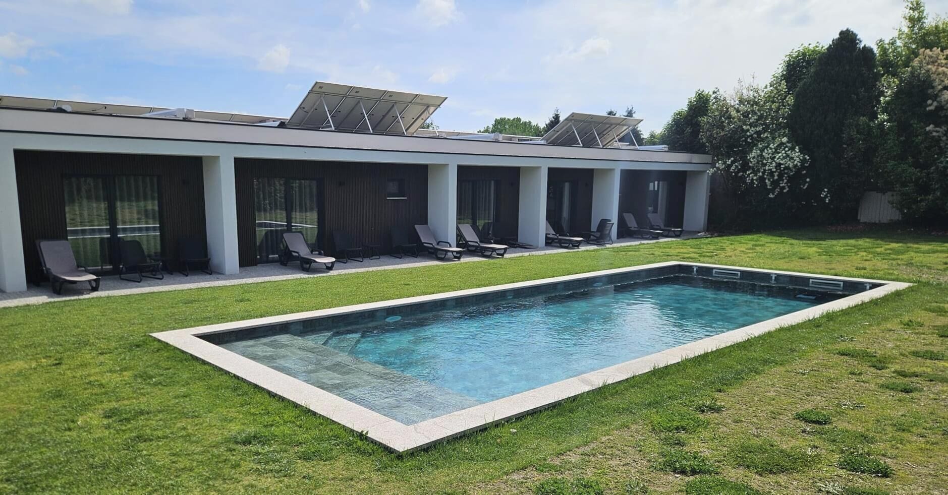 Un bâtiment moderne doté d’une piscine, de chaises longues et de panneaux solaires sur le toit.