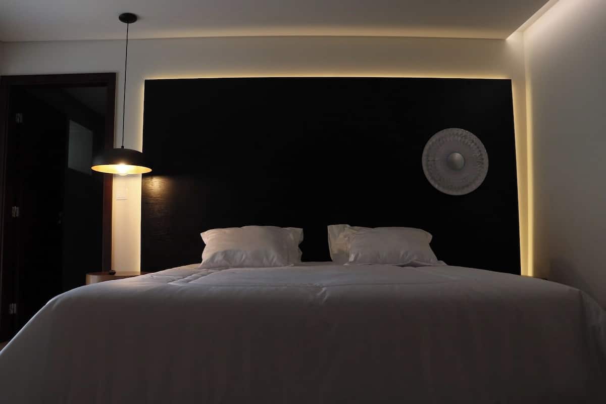 Een slaapkamer met een bed, twee kussens, een bedlampje en een rond object aan de muur.