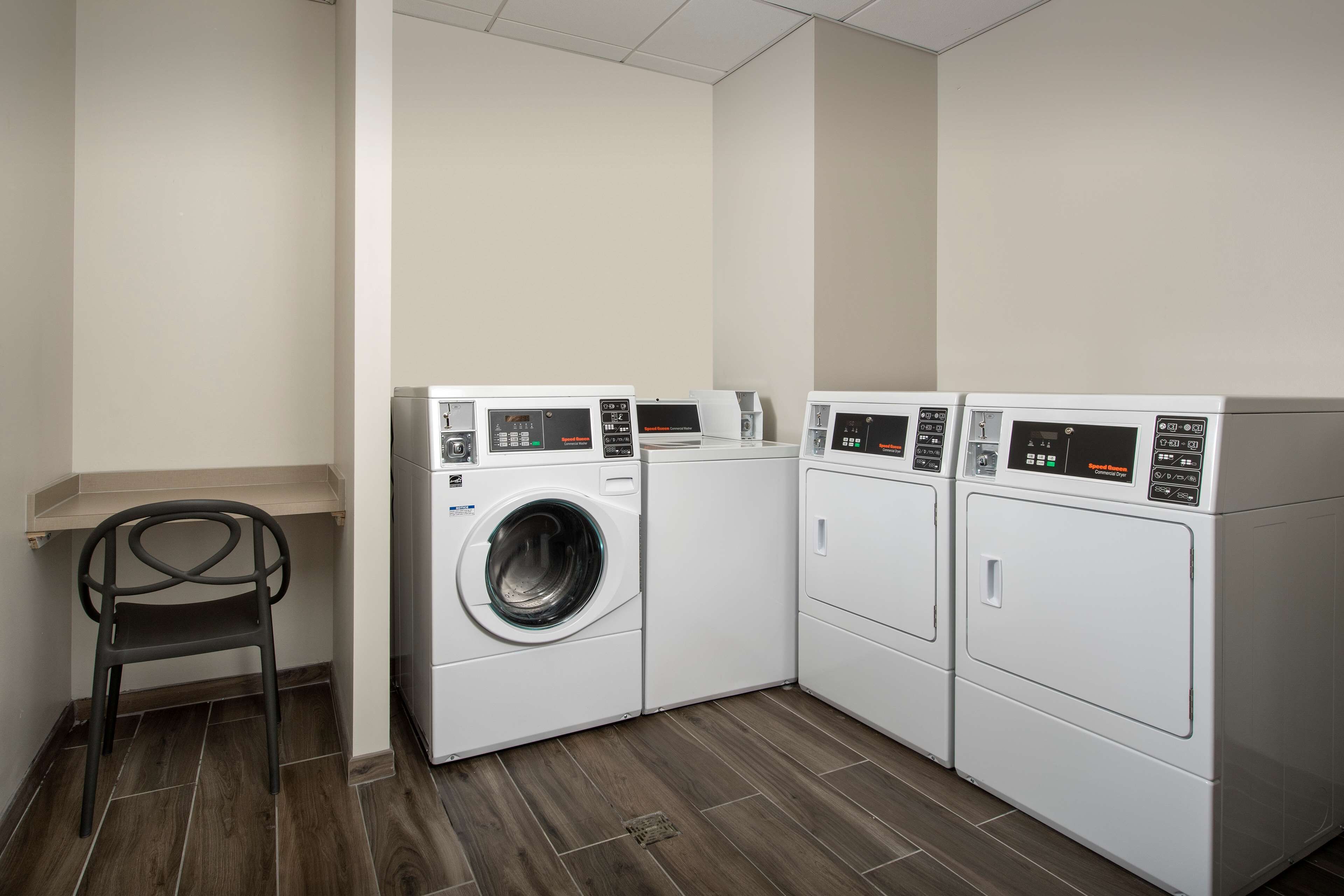 A laundry room with three stacked washing machines and a chair.
