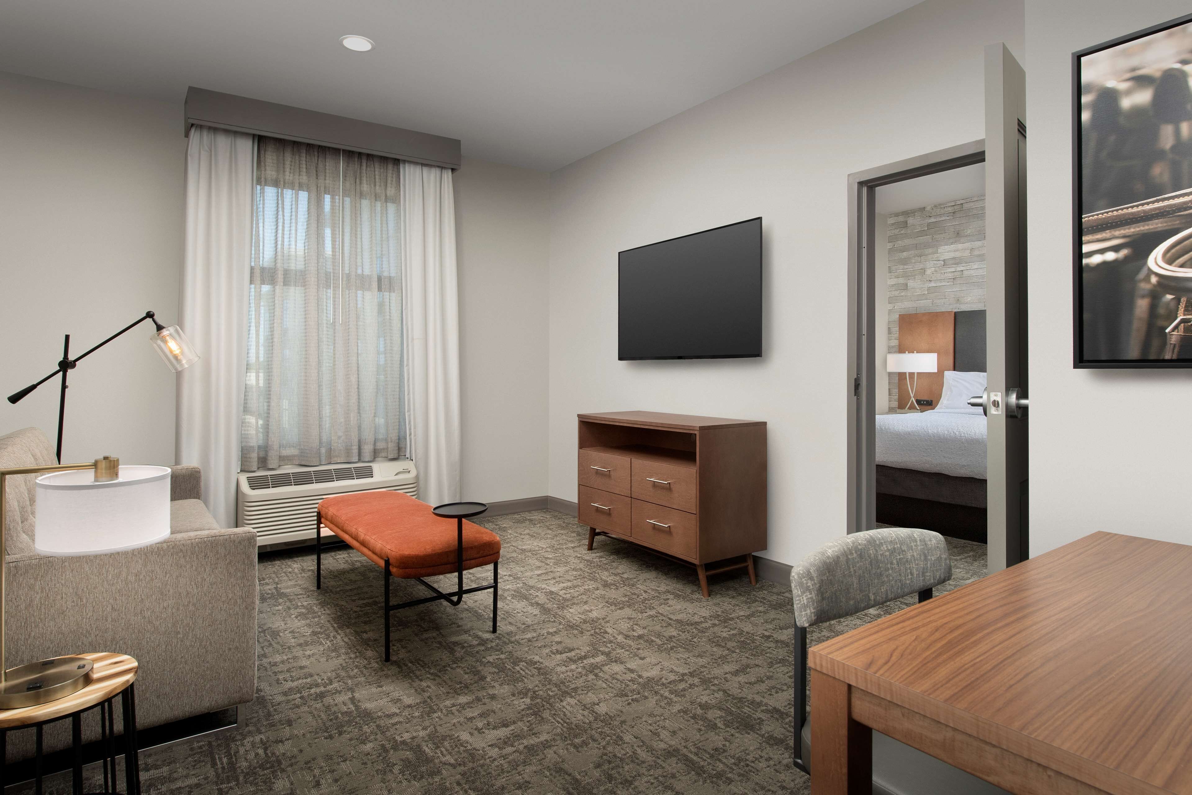 A hotel room with a bed, a desk, a chair, a television, a dresser, and a window with curtains.