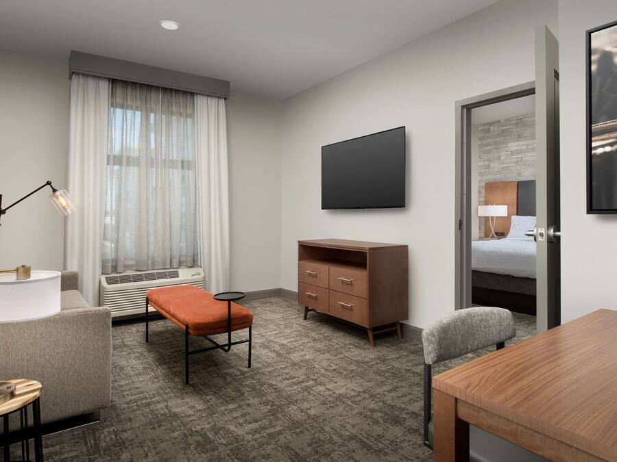 A hotel room with a bed, a desk, a chair, a television, a dresser, and a window with curtains.