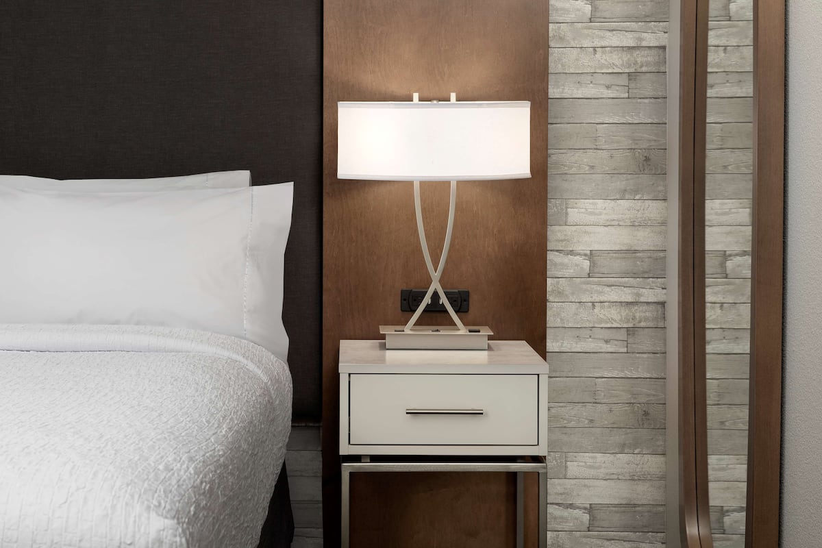 A neatly made bed with white linens, a bedside table with a lamp, and a wooden panel wall.