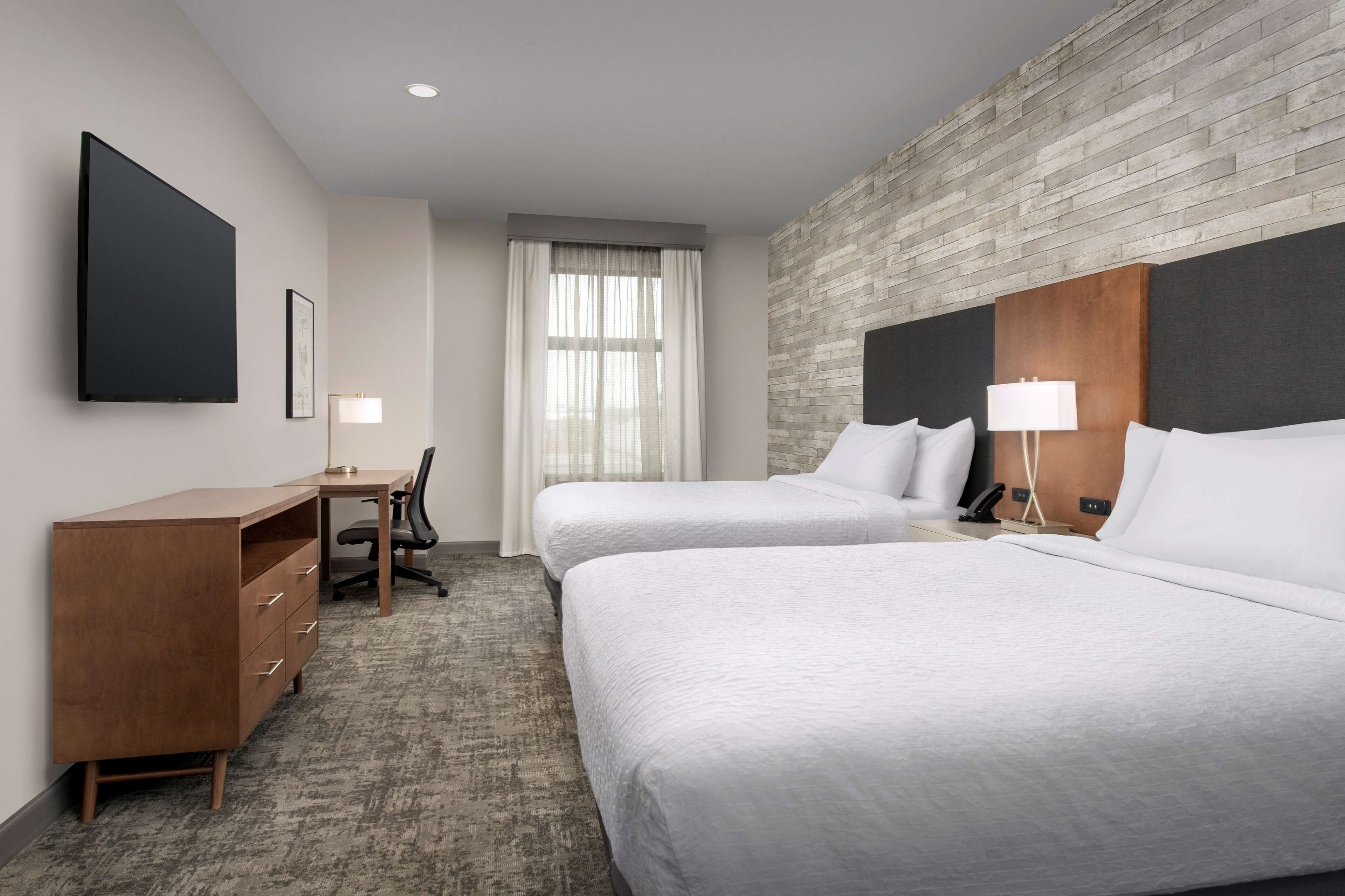 Een hotelkamer met twee bedden, een bureau, een stoel en een groot raam met gordijnen.