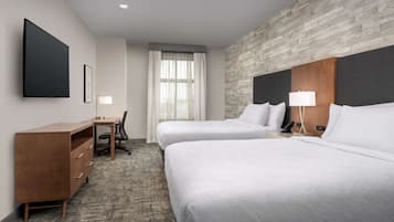 Een hotelkamer met twee bedden, een bureau, een stoel en een groot raam met gordijnen.