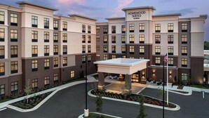 Ett hotell med flera våningar, med en tydlig skylt som visar att det är ett "Homewood Suites by Hilton", ett takförsett utomhusområde med sittplatser och en flaggstång med den amerikanska flaggan.
