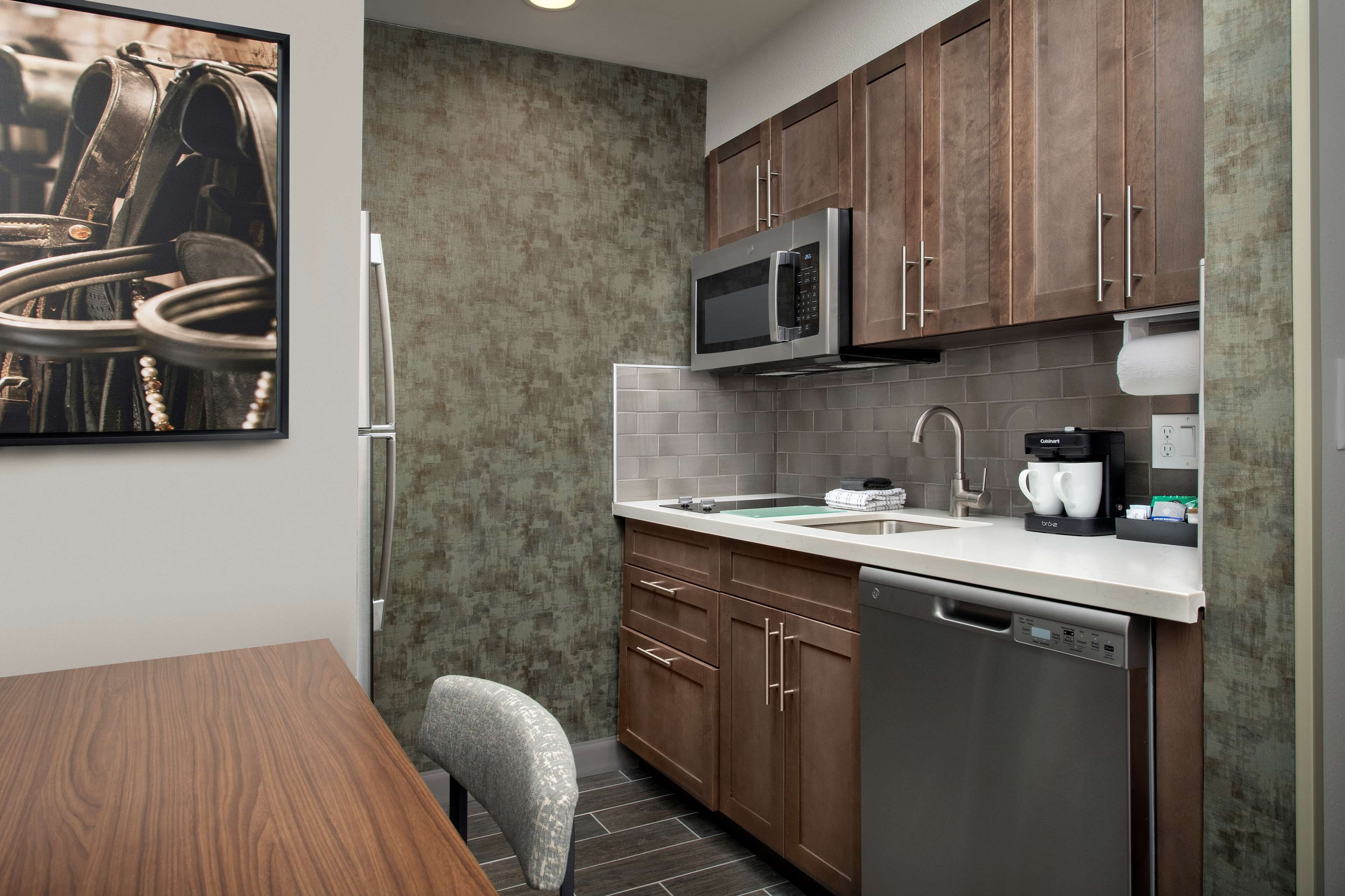 A compact kitchen with wooden cabinets, a stainless steel microwave, a coffee maker, and a dishwasher.