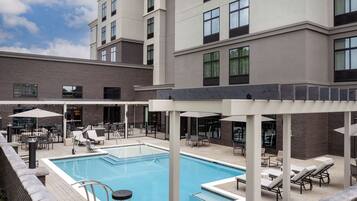 A rooftop pool area with lounge chairs and umbrellas, surrounded by a modern building with large windows.