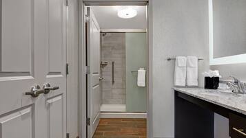 A modern bathroom with a shower, a vanity with a marble countertop, and a large mirror.