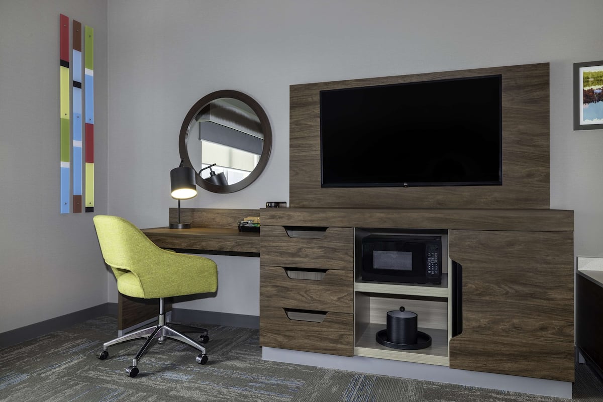 A modern office space with a desk, ergonomic chair, built-in TV, and a microwave.