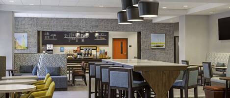 A modern hotel lobby with a bar area, seating arrangements, and a patterned carpet.