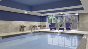 An indoor swimming pool with clear water, a blue and white color scheme, and a seating area with chairs and a plant. - Hampton Inn Midland, On (Midland)