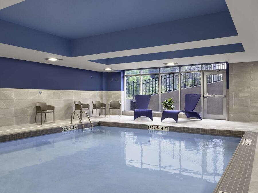 An indoor swimming pool with clear water, a blue and white color scheme, and a seating area with chairs and a plant.