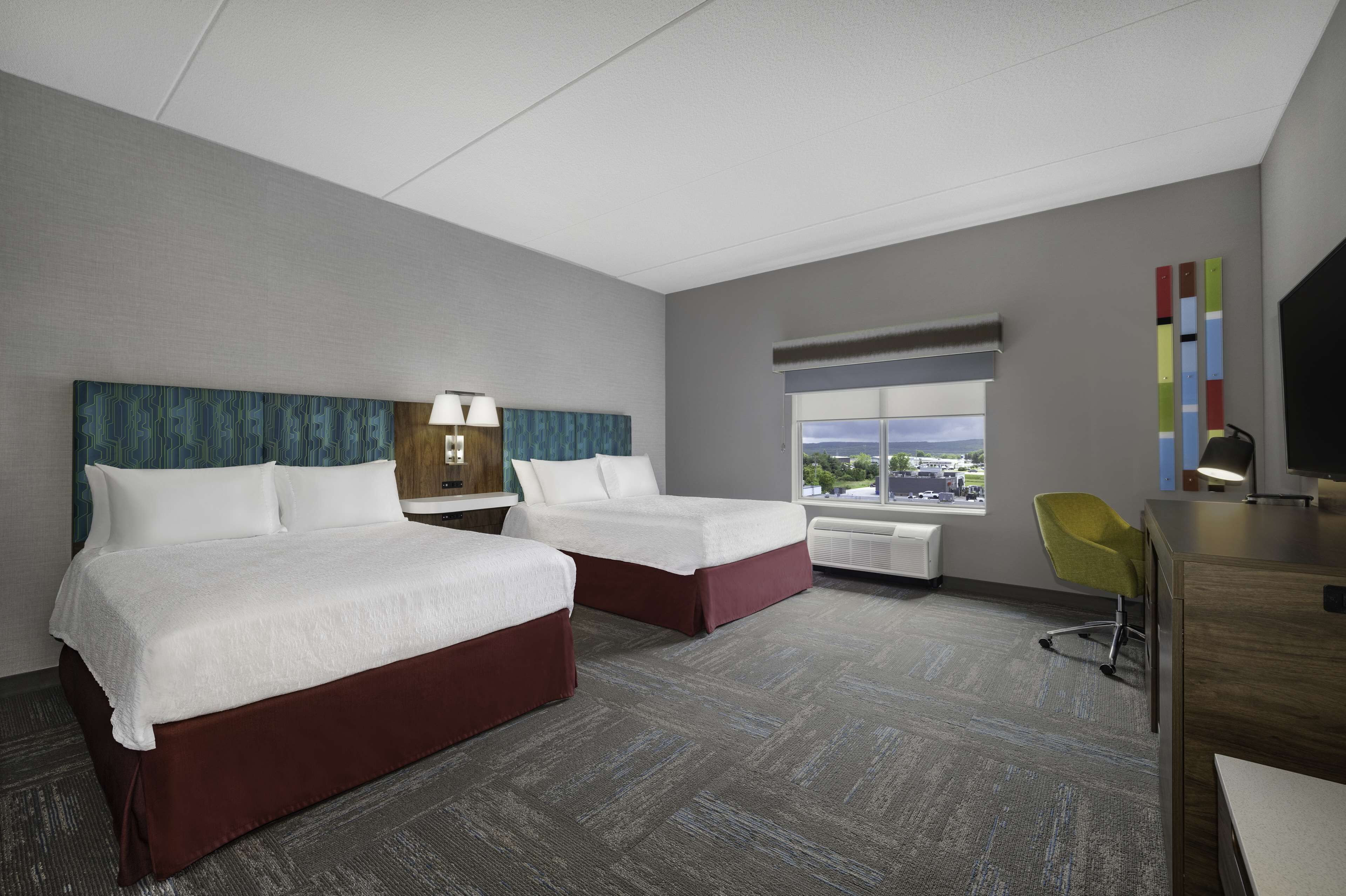 A hotel room with two beds, a desk, a chair, a TV, and a window with a city view.