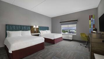 A hotel room with two beds, a desk, a chair, a TV, and a window with a city view.