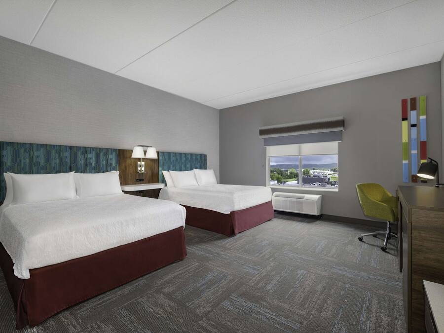 A hotel room with two beds, a desk, a chair, a TV, and a window with a city view.