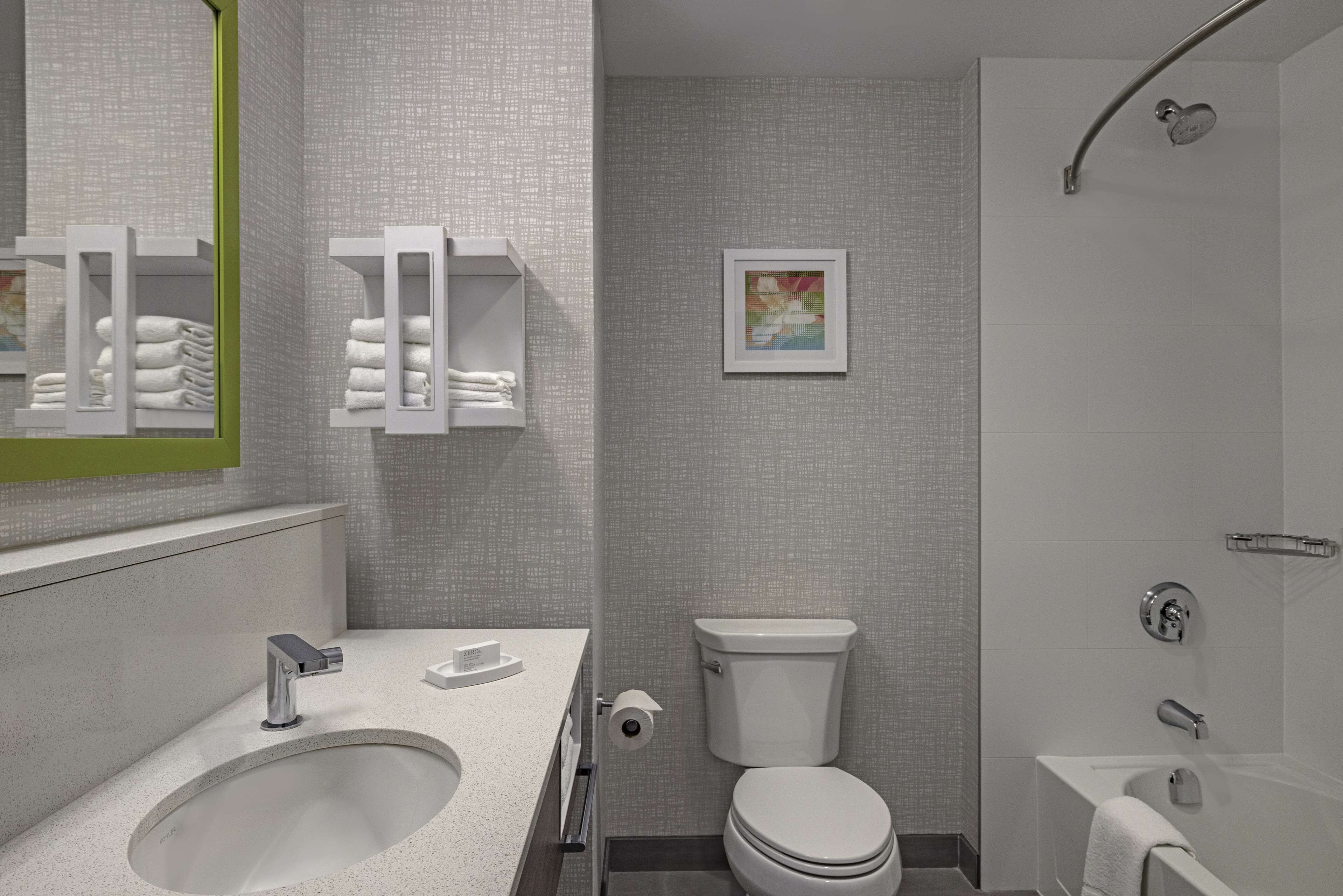 A modern bathroom with a large sink, toilet, and bathtub. There are towel racks and a framed picture on the wall.